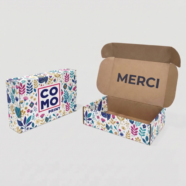 Bo&icirc;te d'exp&eacute;dition personnalis&eacute;e en carton avec motifs floraux color&eacute;s, logo Comoprint et message MERCI &agrave; l'int&eacute;rieur